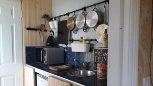 Un angolo cottura funzionale con forno a microonde, bollitore e pentole appese.
