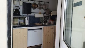 Una cucina compatta con forno a microonde, bollitore, pentole appese e un piccolo frigorifero.