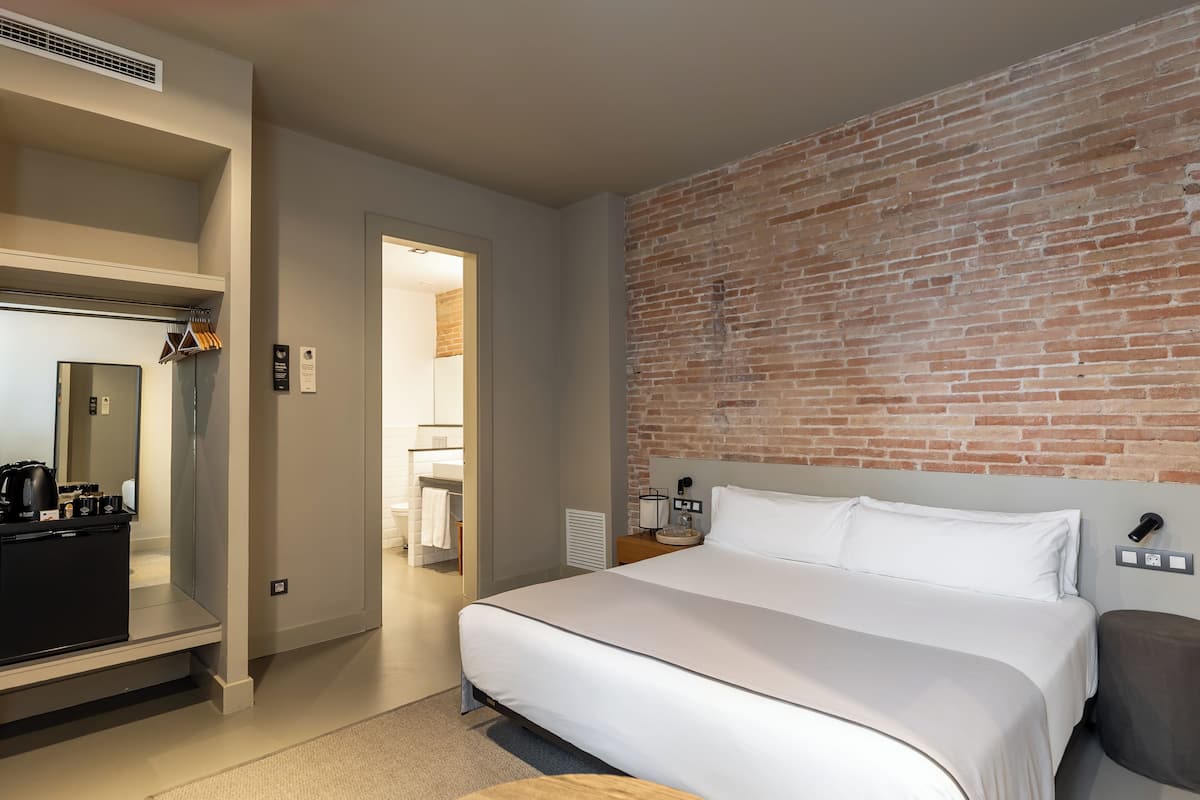 Una habitación de hotel con una cama grande, un armario, un espejo y una pared de ladrillo decorativa.