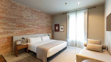 Una habitación de hotel moderna con una pared de ladrillo decorativa, una cama grande, una mesita de noche con una lámpara y vistas al exterior a través de una ventana.