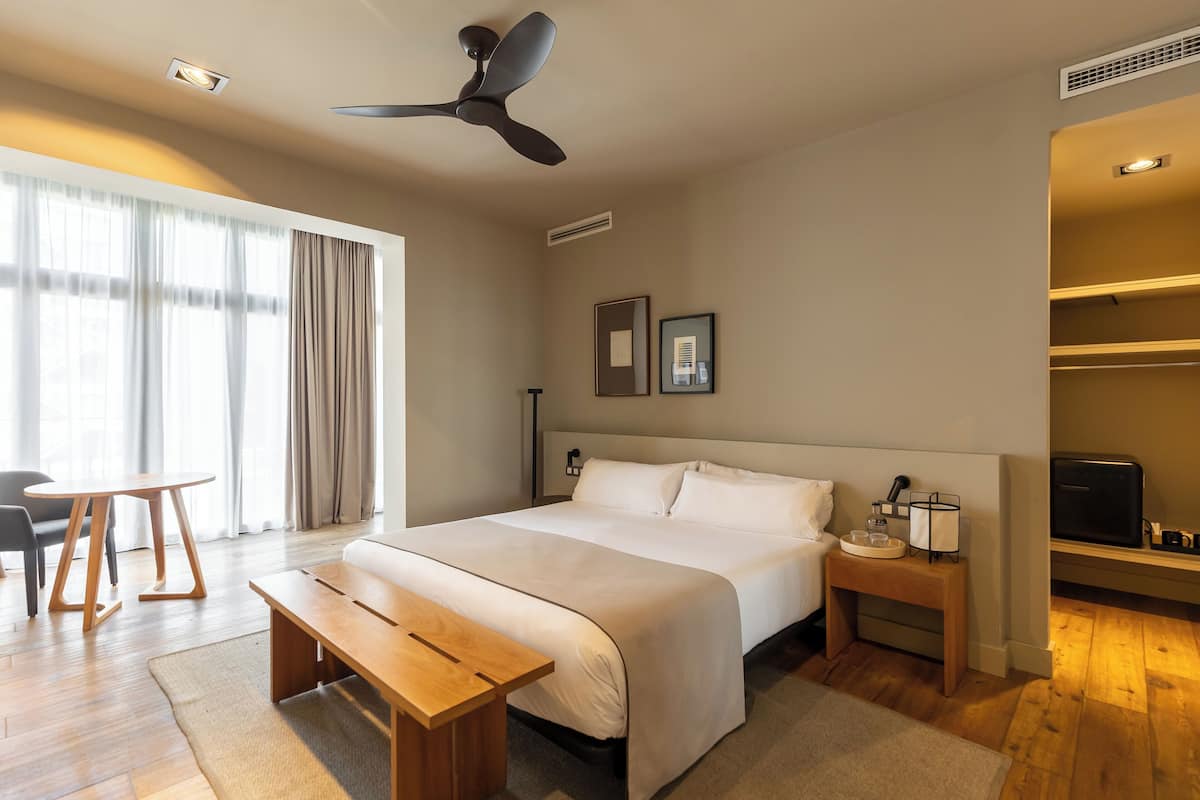 Una habitación de hotel con cama, mesita de noche, lámpara y ventilador de techo.