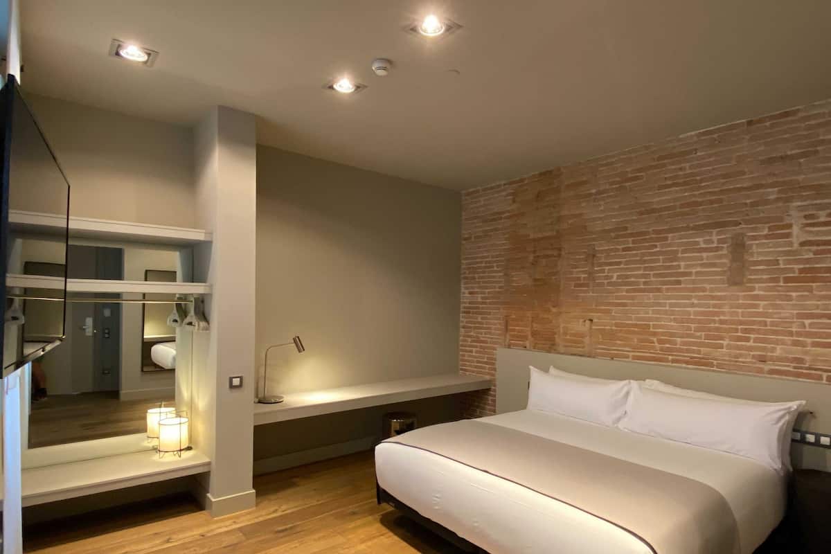 Una habitación de hotel moderna con una cama grande, un tocador con espejo y una pared decorada con ladrillos.