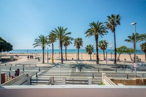 Une promenade en bord de mer bordée de palmiers, un passage piéton et une vue dégagée sur la plage et la mer.
