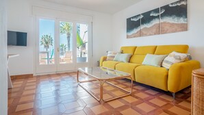 A bright yellow sofa with multiple cushions, a glass coffee table, and a large painting of a beach scene. - See front apartment for 6 (Cambrils)