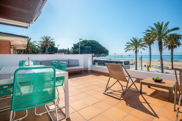 Une terrasse avec une table et des chaises, un canapé et une vue sur la plage et les palmiers.
