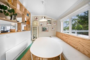 A room with a white table, wooden shelves, and a bench by a window with a view of trees. - Retro Beach Vibes (Lorne)