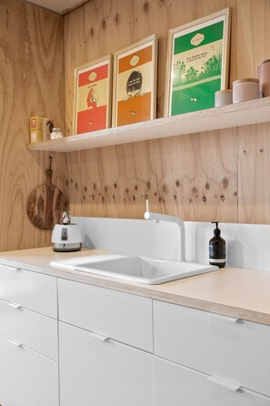 A kitchen with a white countertop, a sink, and a wooden wall. There are three framed posters on a shelf above the countertop.