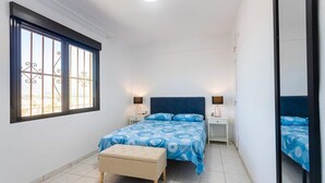 A bedroom with a bed, bedside tables, a bench, and a large window with metal bars. - VIEWS OF THE BAY (l'Alfàs del Pi)