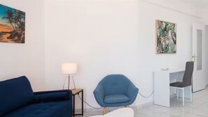 A modern hotel room with a blue sofa, a white coffee table, a blue armchair, a desk with a chair, and a painting on the wall. - VIEWS OF THE BAY (l'Alfàs del Pi)