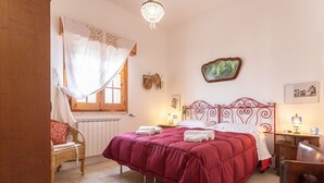 Quarto com cama, cadeira, mesa de cabeceira, abajur e um quadro na parede.