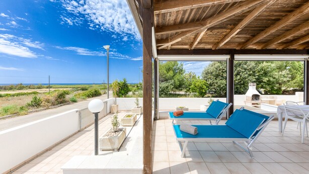 Un espace extérieur abrité comprenant deux fauteuils de jardin bleus, un barbecue et une vue sur la mer.
