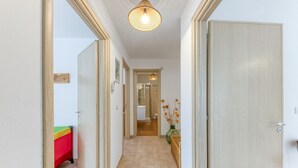 Un couloir avec une porte en bois, un sol carrelé, un luminaire suspendu et une petite table sur laquelle se trouve un vase.