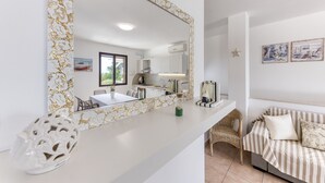 Une cuisine moderne avec des meubles blancs, un grand miroir à cadre doré et un coin repas comprenant une table et des chaises blanches.