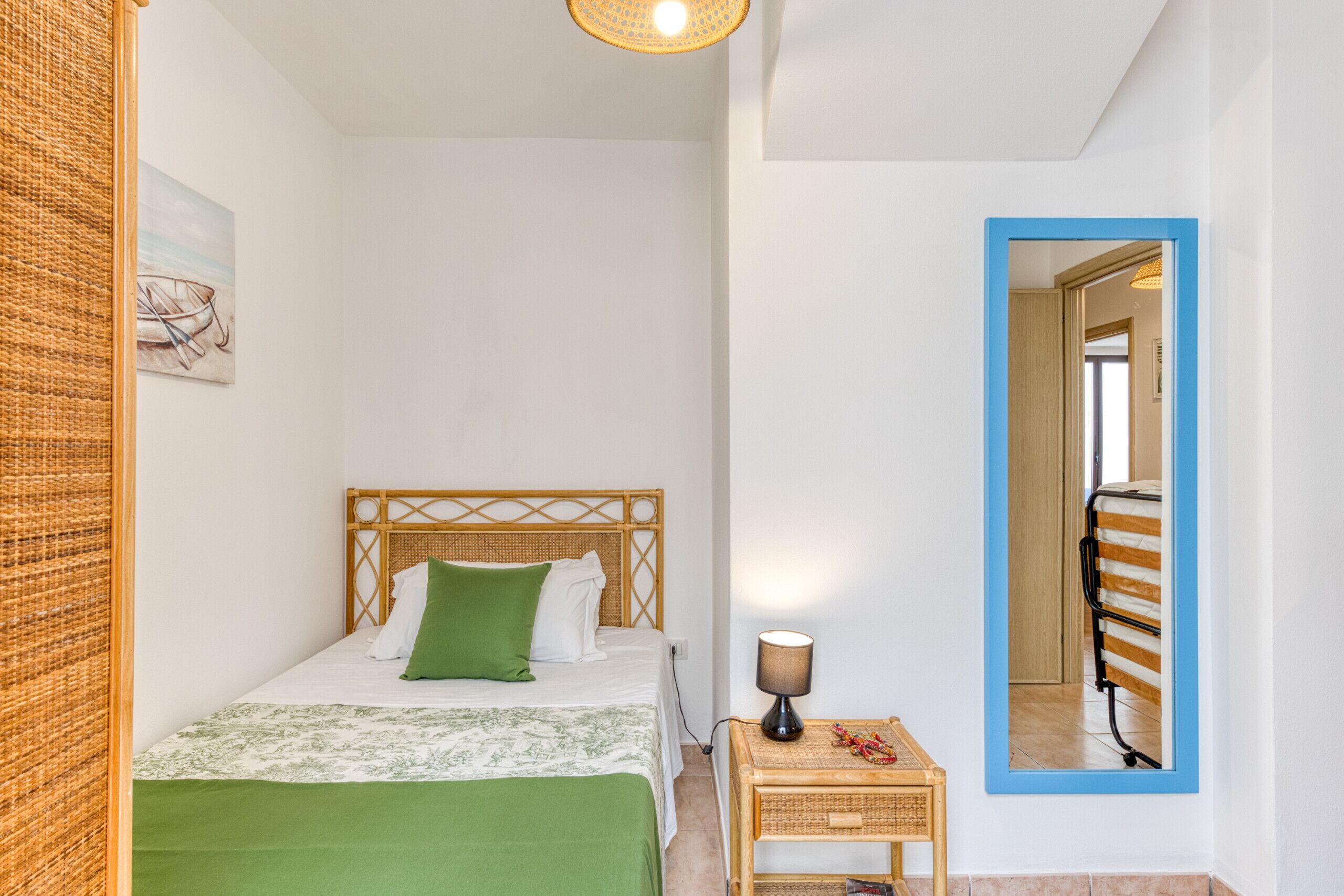 A bedroom with a bed, a bedside table, a lamp, a mirror, and a painting on the wall.