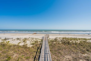 Une promenade en bois qui mène à une plage, sous un ciel dégagé.