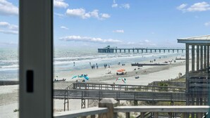 Une vue sur la plage avec une jetée, des personnes se promenant sur la plage et des parasols.