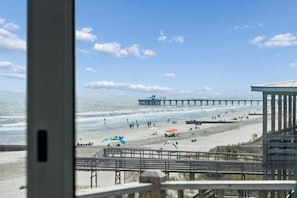 Uitzicht op een strand met een steiger, mensen op het strand en parasols.