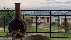 A rustic outdoor grill with a view of a mountain and a white building with red accents in the background. - Moyoni Airport Lodge (Arusha)