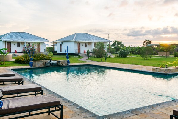 A swimming pool with lounge chairs, two white buildings with blue roofs, and a landscaped garden. - Moyoni Airport Lodge (Arusha)