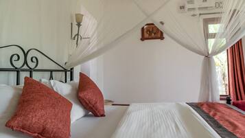 A bedroom with a bed, white bedding, red pillows, a canopy, a wall-mounted clock, and a window with curtains.