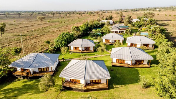 A cluster of cabins with metal roofs, surrounded by lush greenery and fields. - Moyoni Airport Lodge (Arusha)