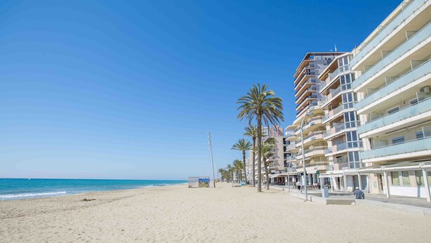 Een strand met een rij meerverdiepingen, palmbomen en een helderblauwe lucht.