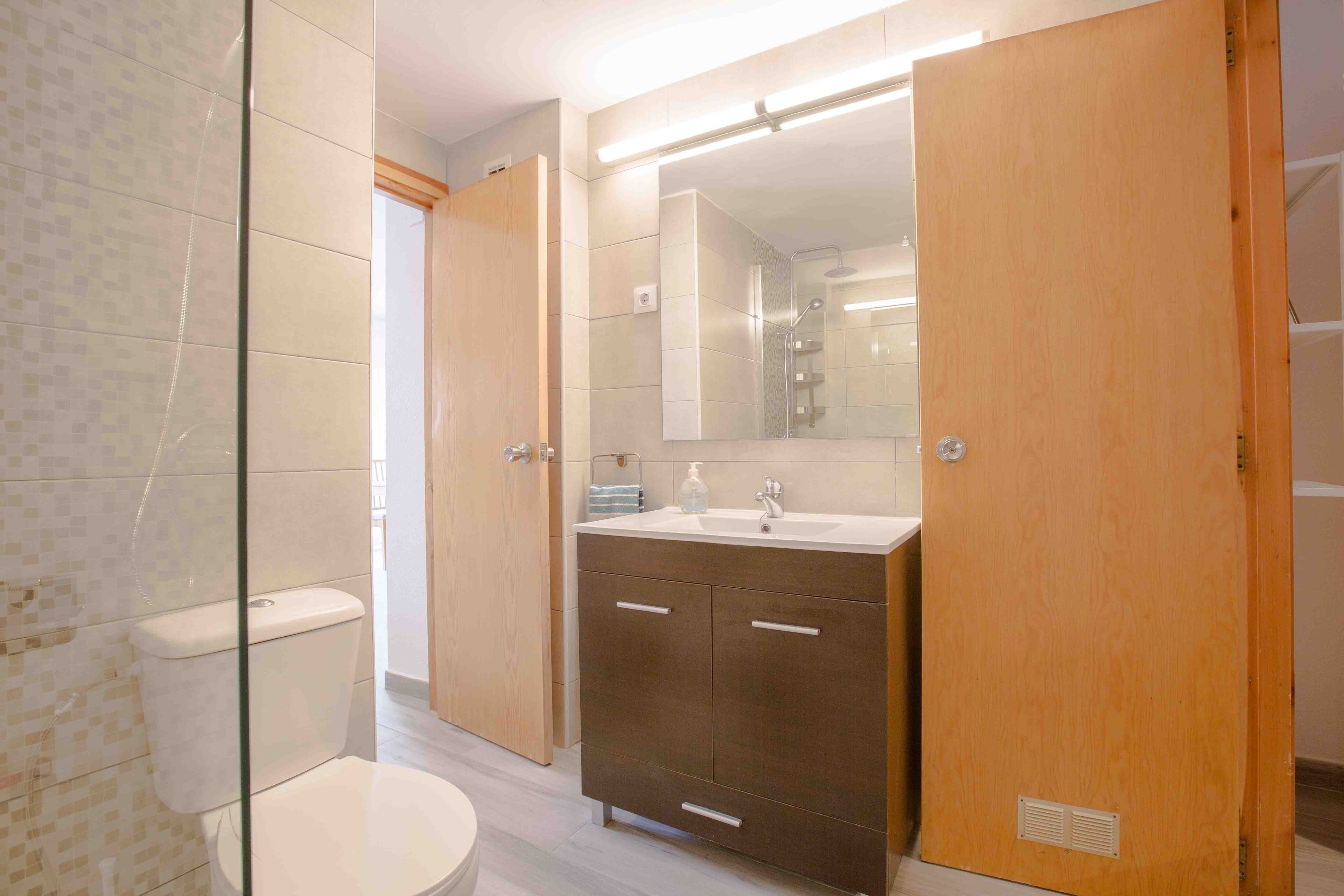 A modern bathroom with a glass shower enclosure, a toilet, a wooden vanity with a mirror, and a sink.