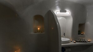 Un baño moderno con un lavabo redondo, un espejo y una ventana pequeña. Hay velas en el suelo y un perchero con toallas.