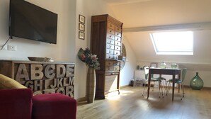 A living room with a red sofa, a wooden cabinet with drawers, a flat-screen TV, and a large window with natural light. - It is a newly renovated attic located in a building from the early 1900s (Milano)