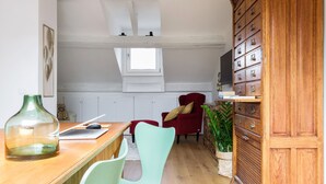 A kitchen with a wooden countertop, a red chair, a green chair, a wooden cabinet with drawers, and a window above the cabinets. - It is a newly renovated attic located in a building from the early 1900s (Milano)