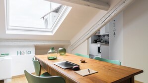 A dining area with a wooden table, green chairs, a laptop, a notebook, and a small cake. A skylight provides natural light. - It is a newly renovated attic located in a building from the early 1900s (Milano)