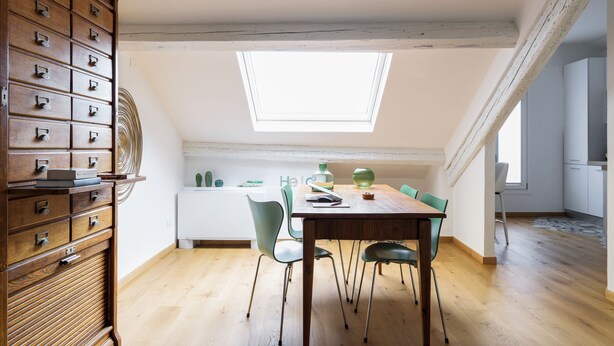 A dining area with a wooden table, green chairs, and a skylight above. - It is a newly renovated attic located in a building from the early 1900s (Milano)