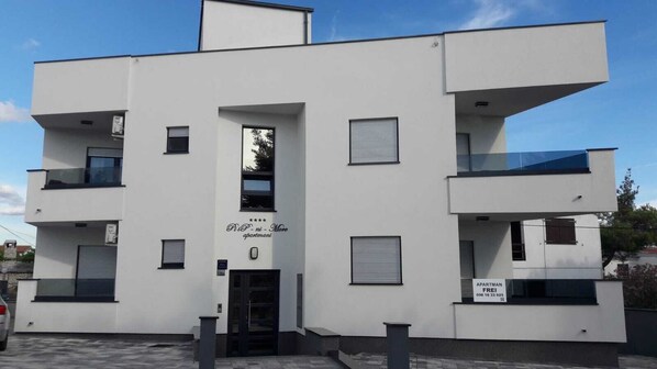 Un immeuble moderne à plusieurs étages, doté d’une façade plate, de balcons et d’une enseigne indiquant qu’il s’agit d’un complexe d’appartements.