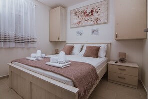 A neatly made bed with towels, a bedside lamp, and a small nightstand with a phone. - Apartments PiiP-ni-More (Vodice)