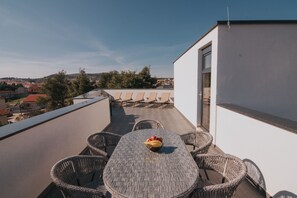 A rooftop terrace with a round table and wicker chairs, a bowl of fruit, and a view of the cityscape. - Apartments PiiP-ni-More (Vodice)