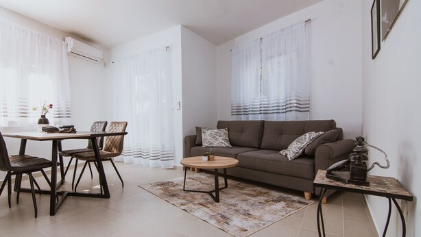 A modern living room with a sofa, coffee table, and dining area with chairs. - Apartments PiiP-ni-More (Vodice)