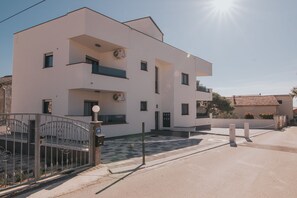 Un bâtiment moderne à deux étages, doté d’un toit plat, d’une entrée sécurisée par un portail et d’une cour dallée.