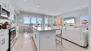 A modern kitchen with white cabinetry, a large island, and a view of the beach.