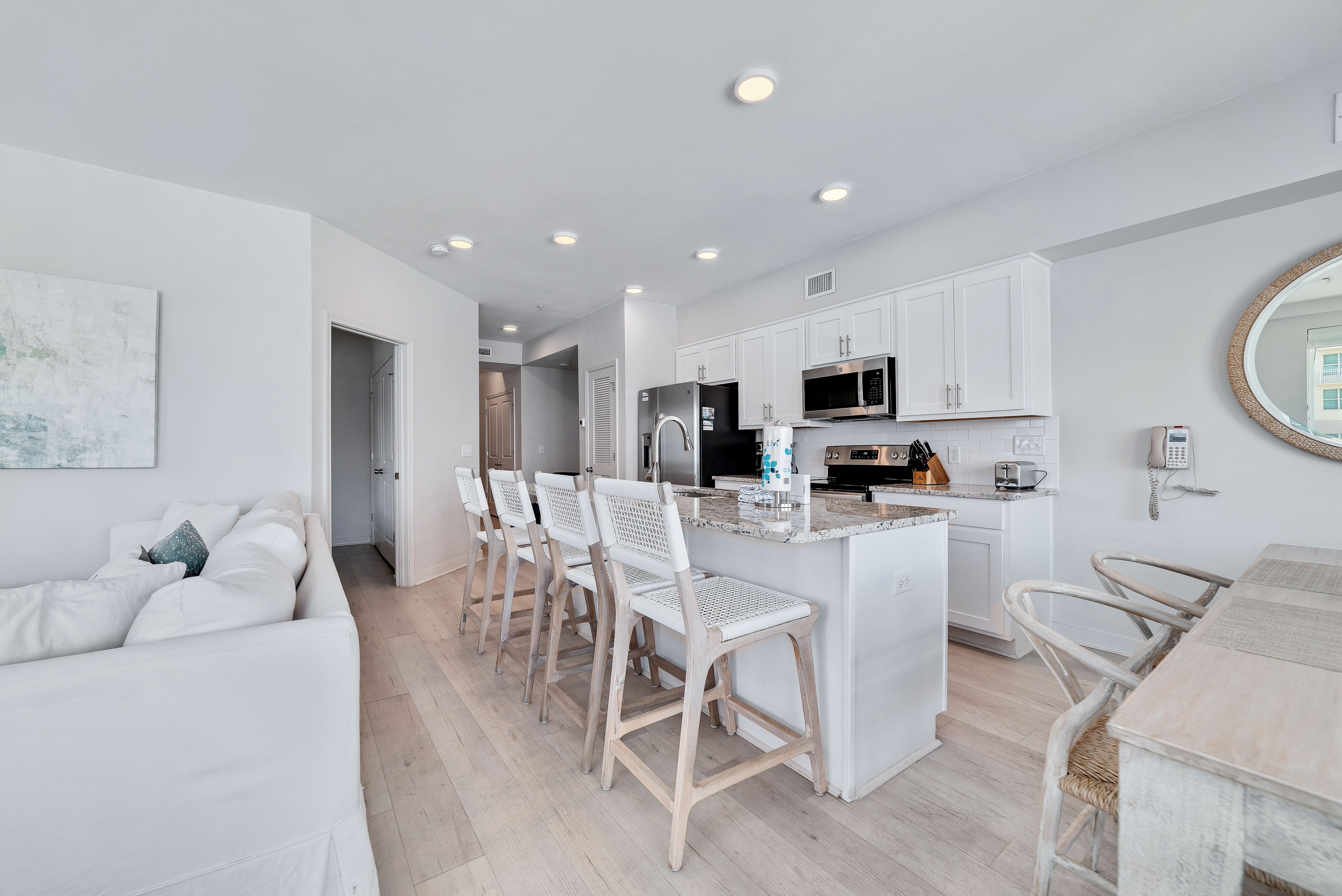 A modern kitchen with white cabinetry, a central island with bar stools, and a dining area with a table and chairs.