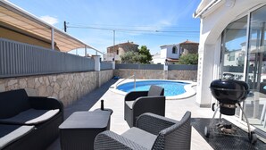 A poolside area with wicker furniture, a barbecue grill, and a stone wall.