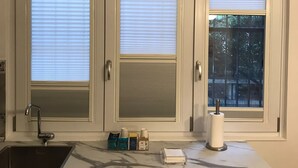 A kitchen with three white cabinets, a sink, and a window with blinds.
