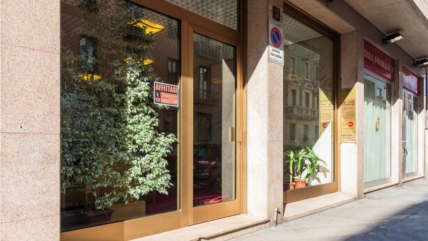 A building with large windows, a sign indicating a no parking zone, and a potted plant outside.