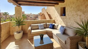 A covered outdoor seating area with a wicker sofa, a glass coffee table, and potted plants. - Attic apartment in Vera Beach with beautiful sea and mountain views (Vera Playa)
