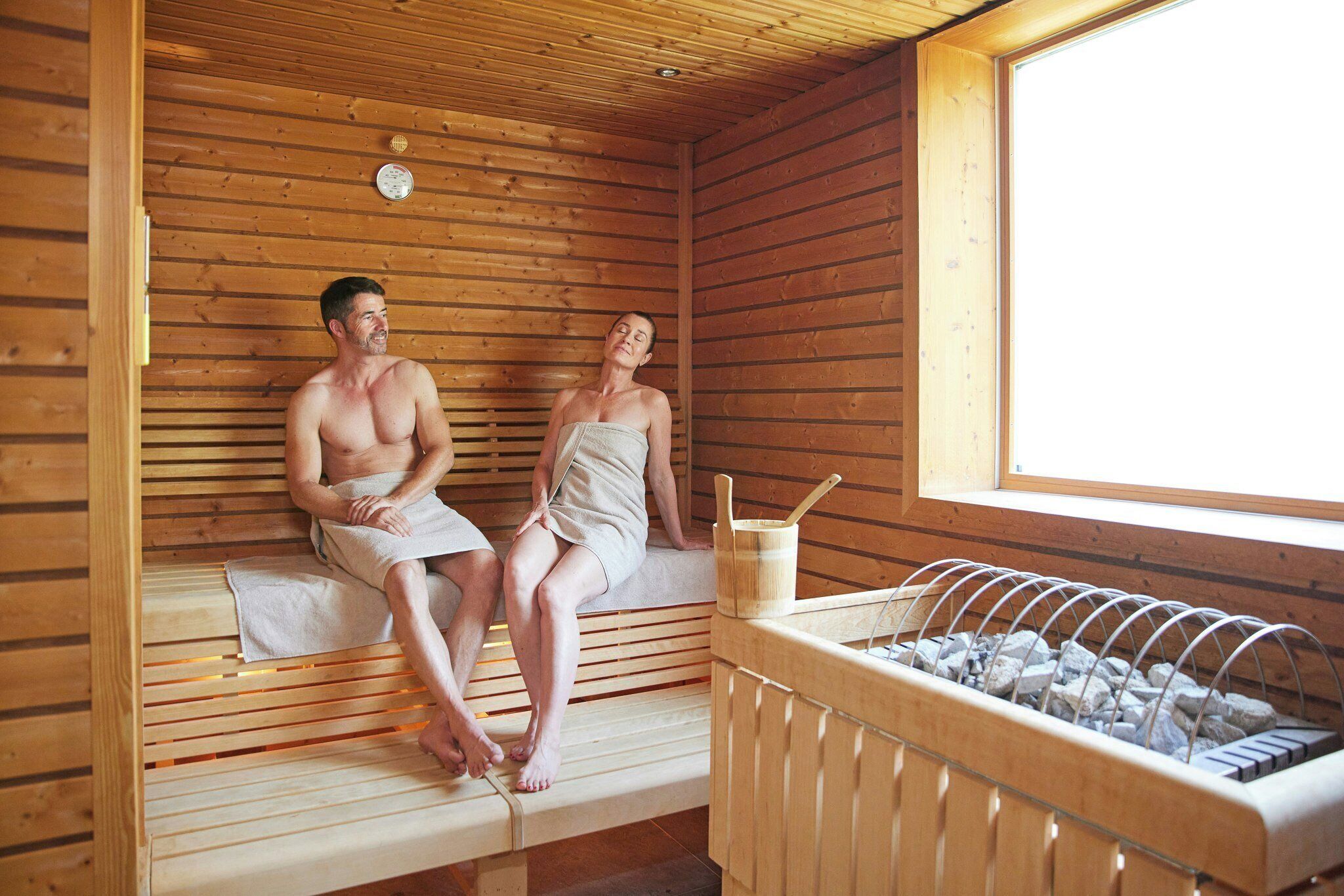 A sauna room with wooden benches, a bench heater, and a window.
