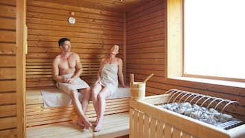 A sauna room with wooden benches, a bench heater, and a window.