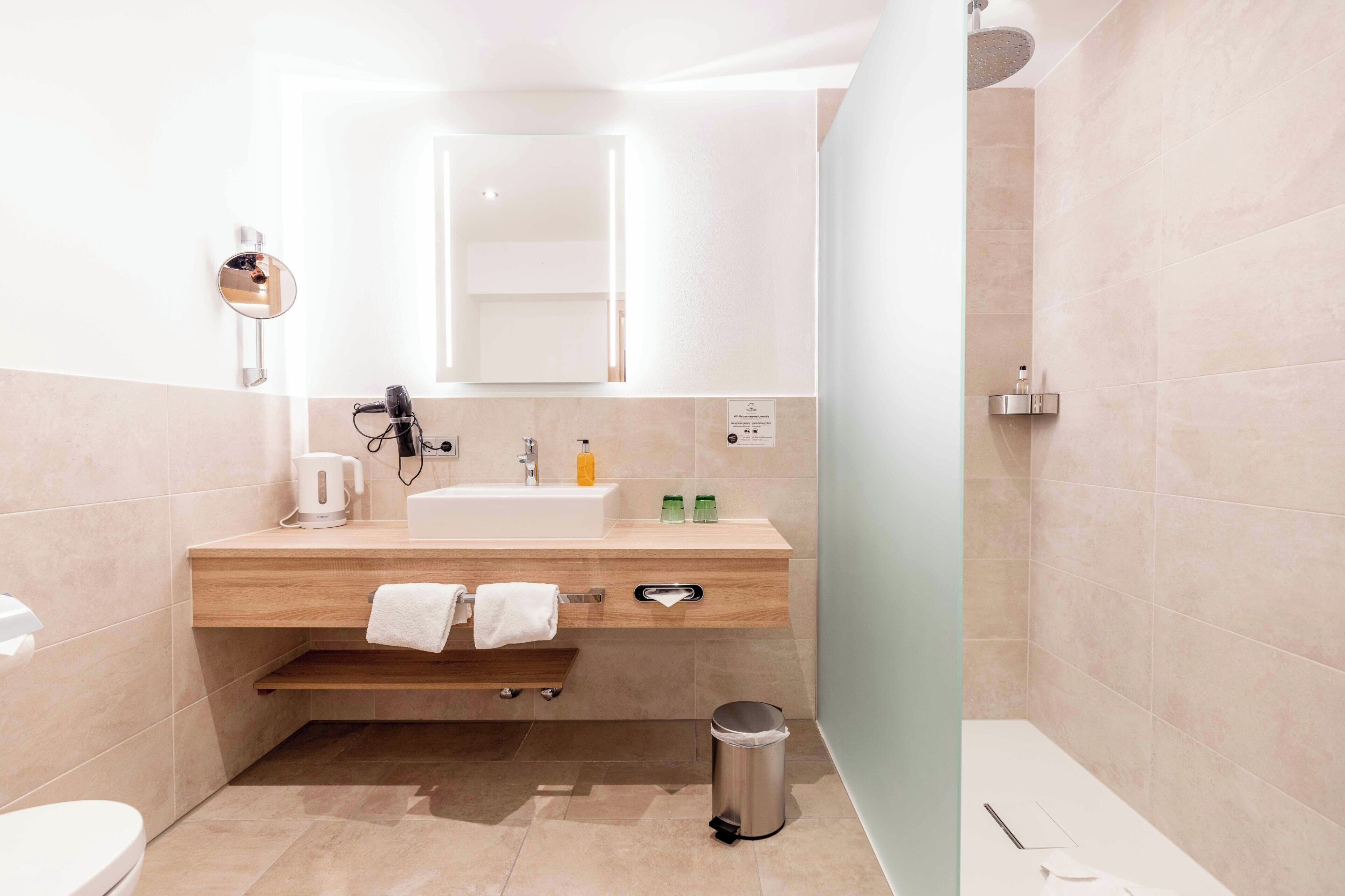 A modern bathroom with a sink, mirror, towel rack, and shower.