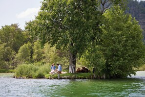 A couple sitting on a grassy island surrounded by water and trees. - Das Walchsee Resort (Walchsee)