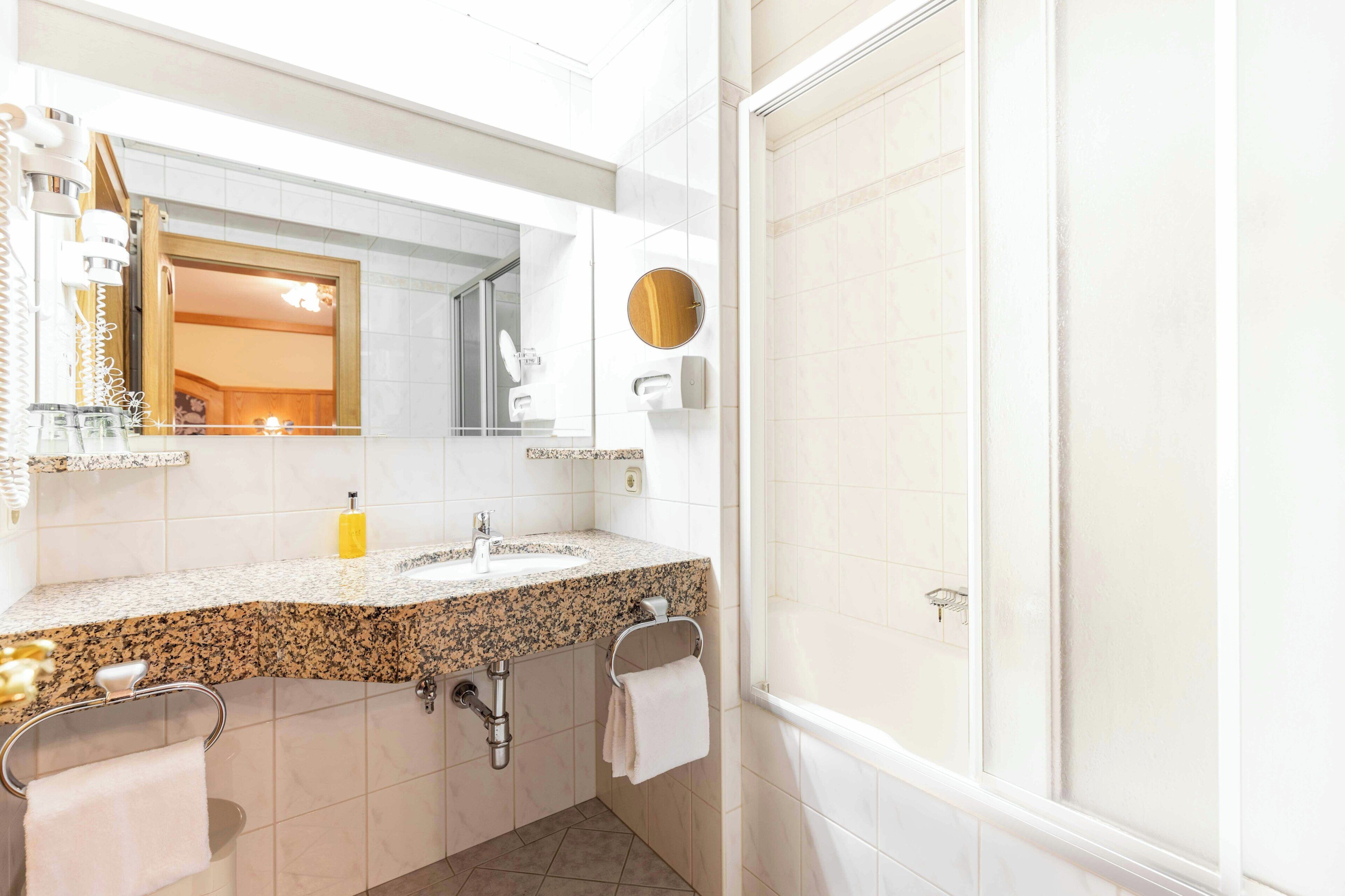 A bathroom with a granite countertop, a sink, a mirror, a towel rack, and a shower area.