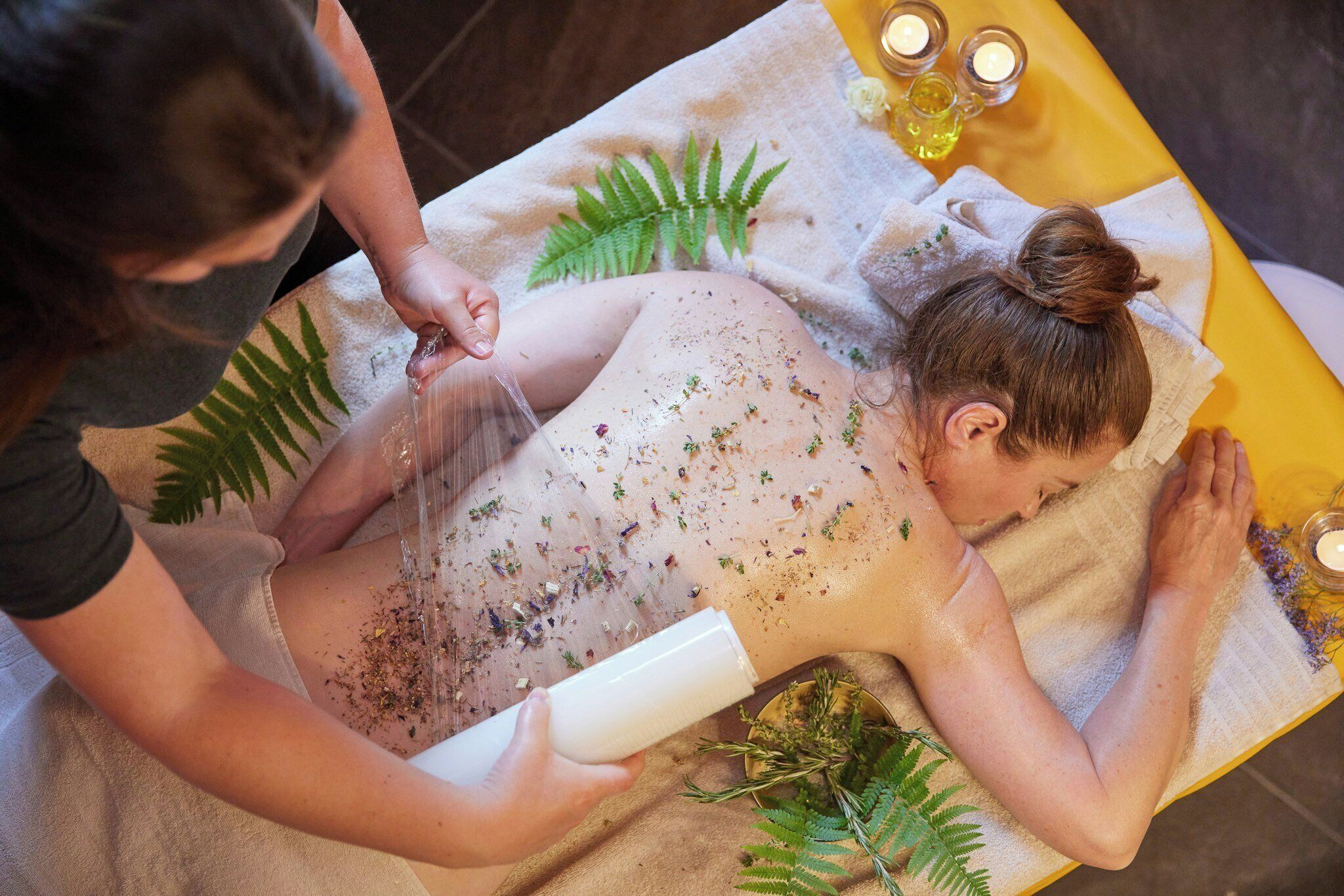 A person receiving a massage with a towel, a bottle, and a plant on a table.