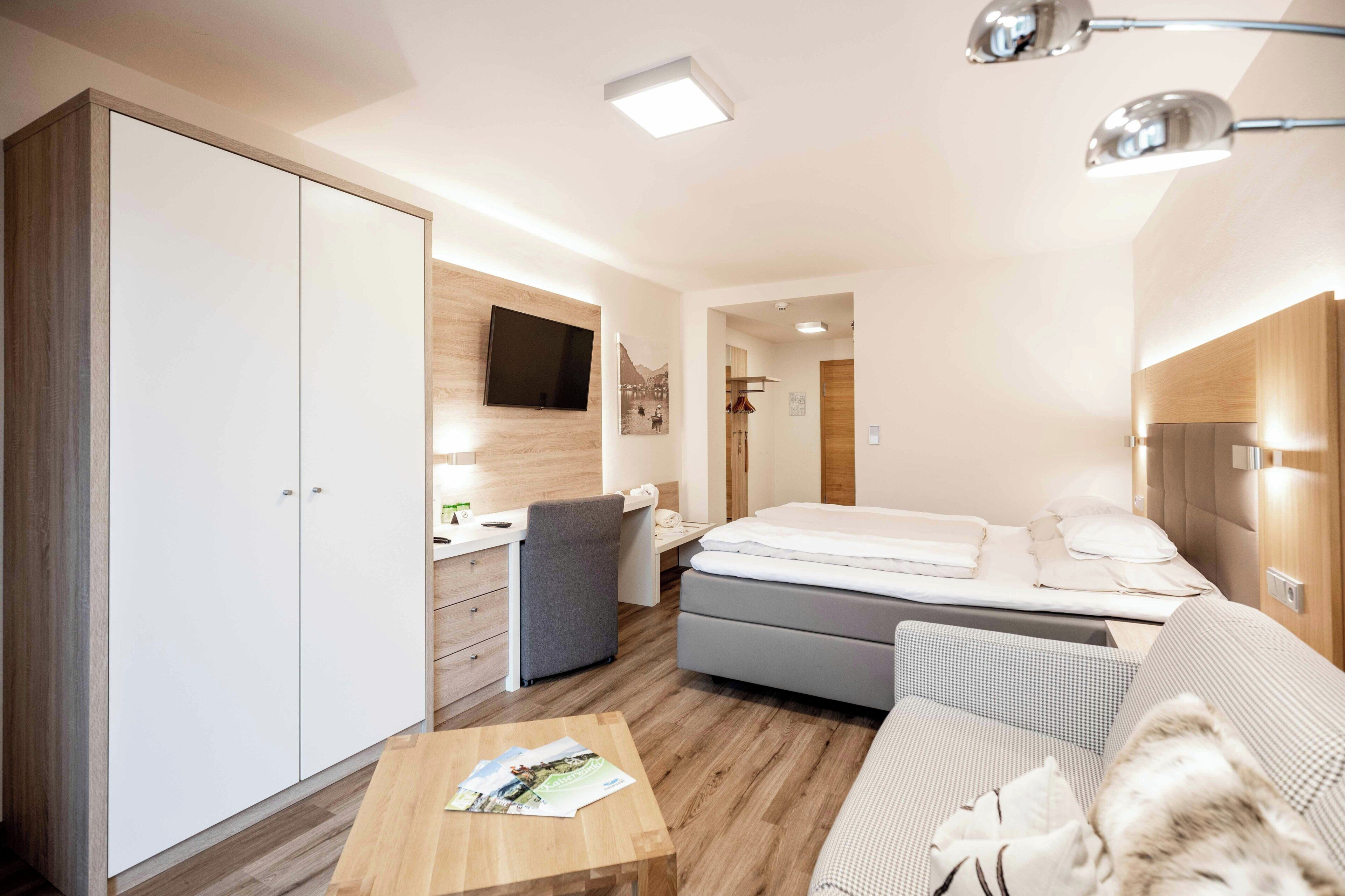 Una habitación de hotel moderna con cama, sofá, escritorio, armario y televisor.